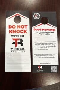 Two T-Rock Roofing door hangers on a dark tabletop. One says