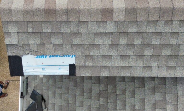 Aerial view of a roof with a damaged section exposing underlayment. A man stands on the ground next to a white car, looking up at the roof—DFW’s trusted experts for roof repairs can help restore your home’s safety.