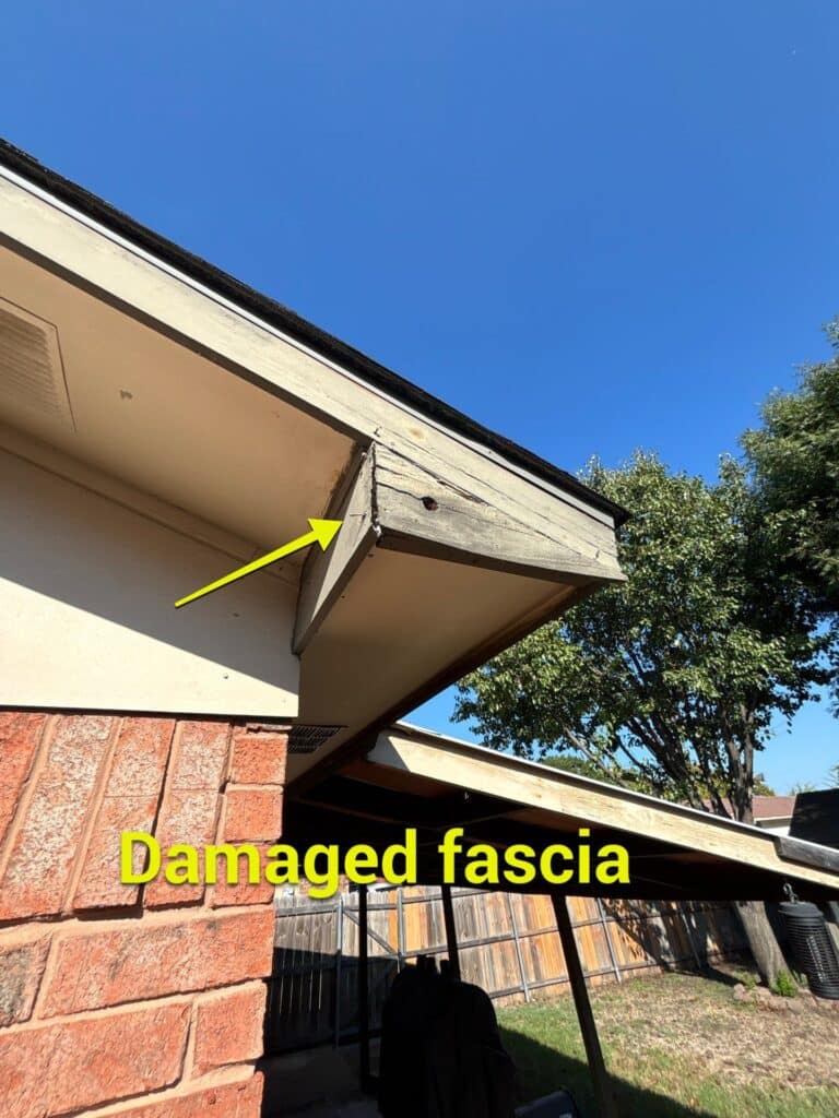 A house roof corner with a wooden fascia board that is damaged and weathered. A yellow arrow points to the fascia, and large yellow text reads "Damaged fascia." Trees and a fence are in the background—perfect for Fascia services or gutter repair. - T Rock Roofing and Contracting A house roof corner with a wooden fascia board that is damaged and weathered. A yellow arrow points to the fascia, and large yellow text reads "Damaged fascia." Trees and a fence are in the background—perfect for Fascia services or gutter repair.